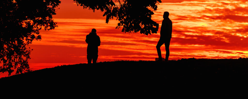 two men on a hill during sunset